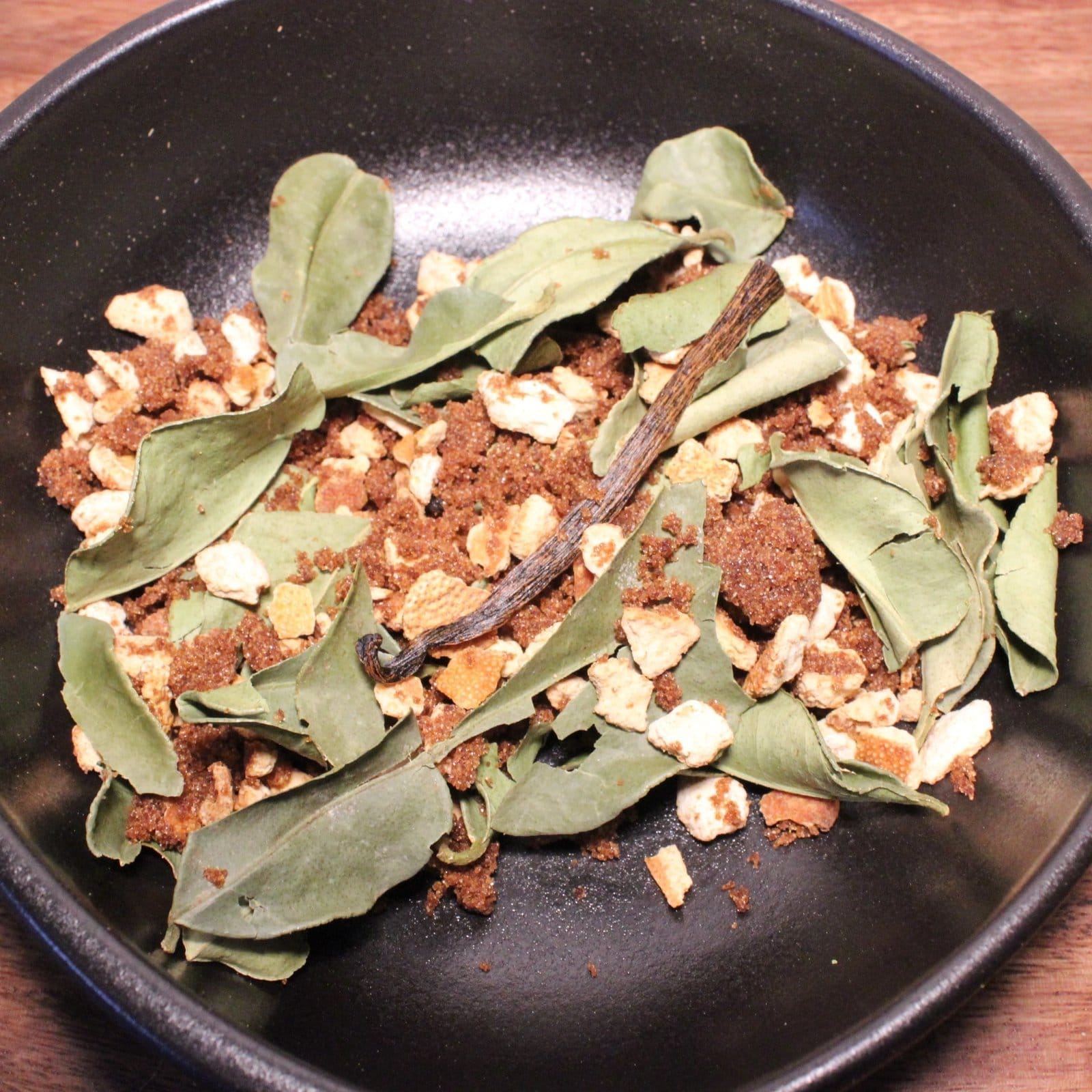 Mélange d'épices et herbes, feuilles et écorces séchées dans un bol noir, pour cuisine aromatique et saveurs exotiques.
