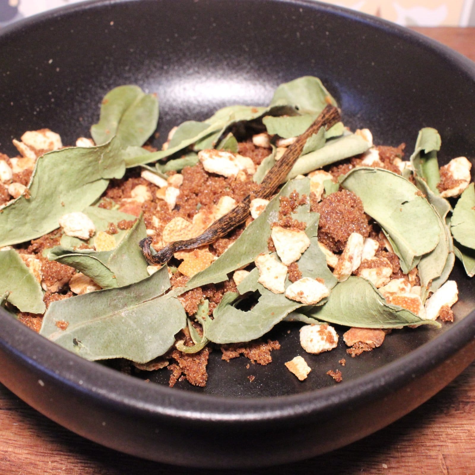 Mélange d'épices et herbes séchées dans un bol noir pour infusion ou cuisine aromatique.
