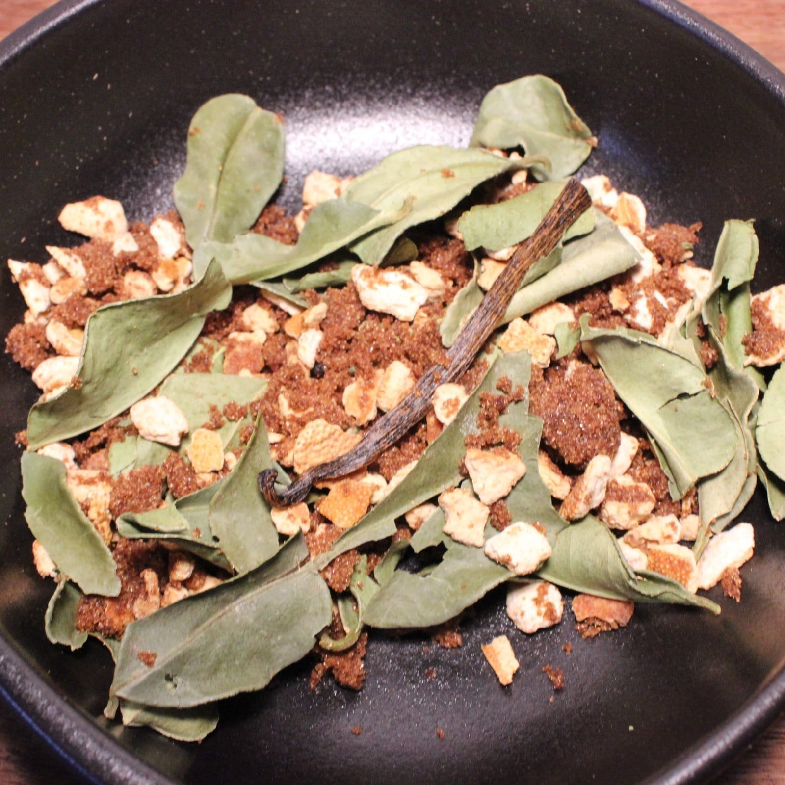 Épices et feuilles fraîches dans un bol noir pour infusion aromatique ou recette exotique.