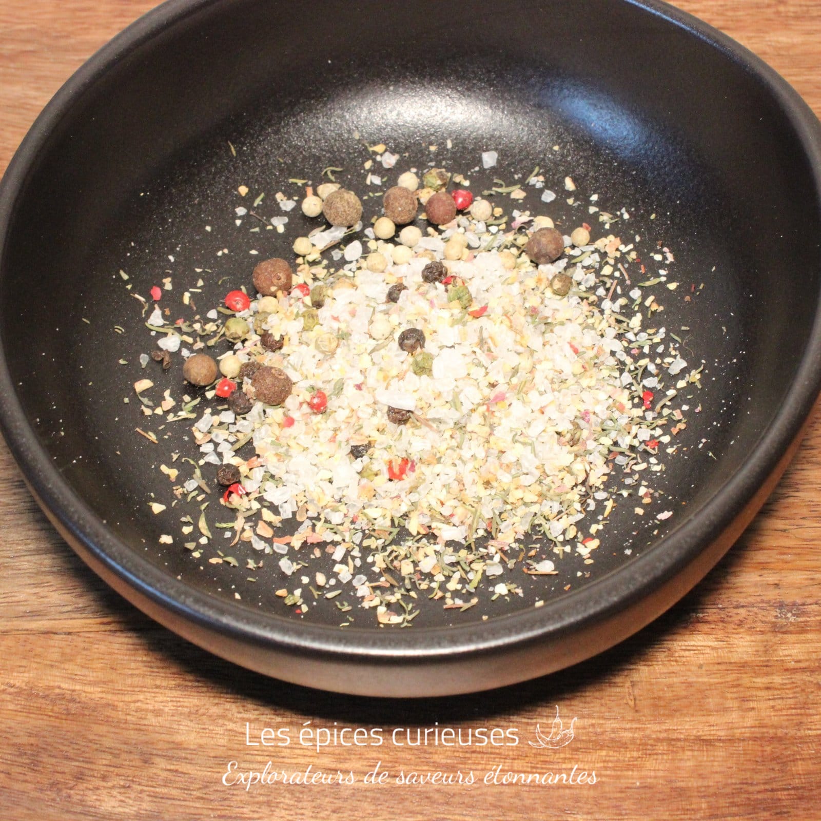 Assortiment d'épices colorées dans un bol noir sur une table en bois. Mélange parfait pour rehausser vos plats.