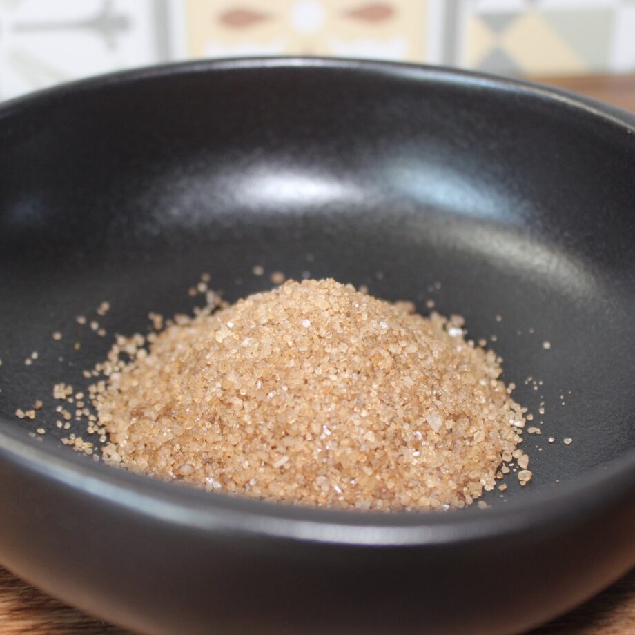 Sucre de canne brun dans un bol noir, idéal pour pâtisserie et boissons. Texture granuleuse et couleur riche.