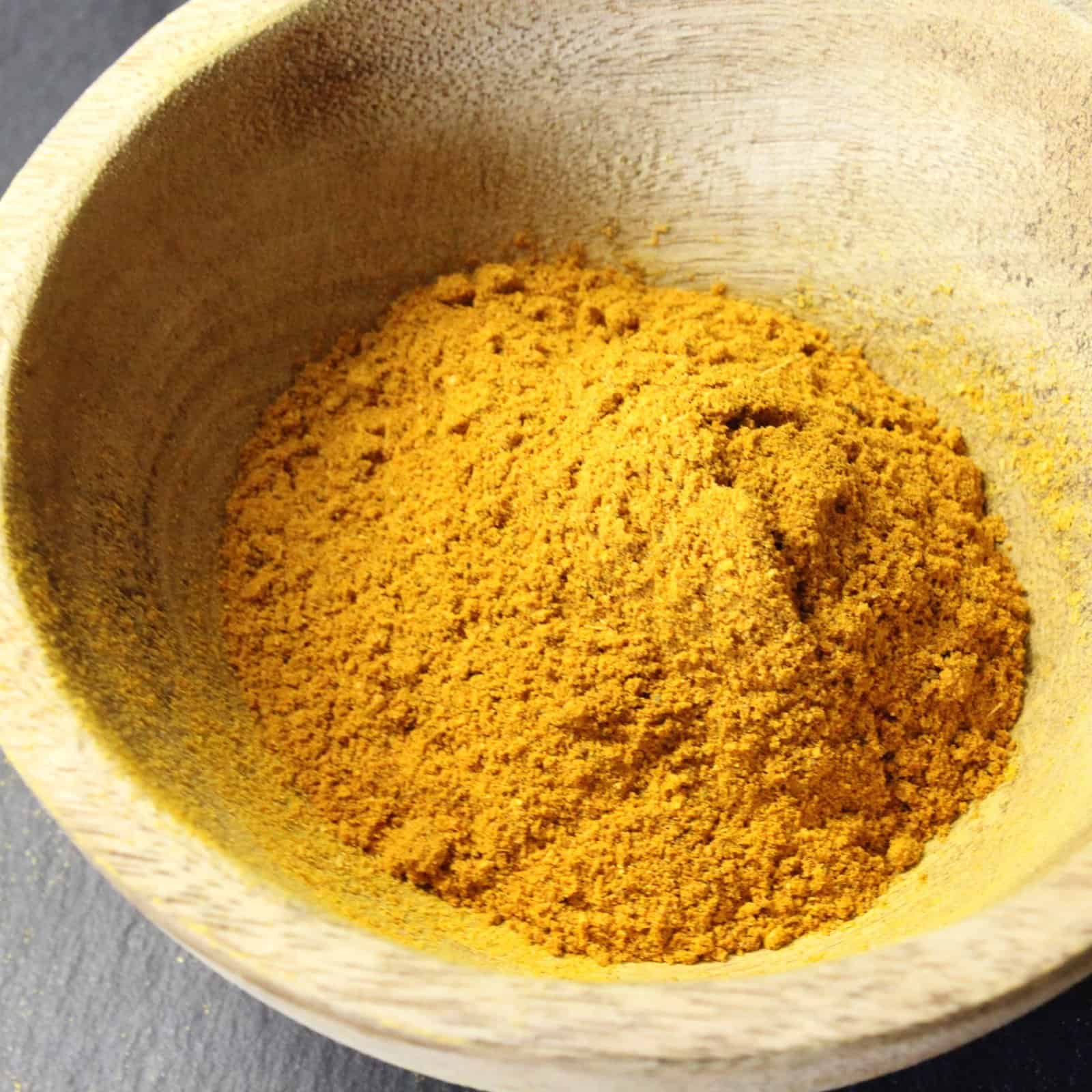 Poudre d'épices Tikka Massala dans un bol en bois, idéale pour cuisine indienne.