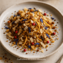 Assiette de crumble avec des copeaux de noix de coco, baies rouges et fleurs bleues sur un plat en céramique.