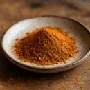 Poudre de cannelle dans un bol en céramique sur une table en bois, idéale pour la cuisine et les boissons chaudes.