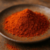Poudre de paprika rouge épicé dans une assiette en céramique sur une table en bois.