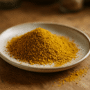 Assiette en céramique avec poudre de curcuma dorée, sur une table en bois rustique.