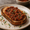 Toast garni de sauce tomate parfumée et de basilic frais sur une assiette en céramique.