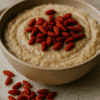 Bol de porridge crémeux garni de baies de goji rouges sur une assiette en céramique rustique.
