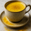 Tasse de latte au curcuma épicé sur soucoupe avec poudre de curcuma, posée sur une surface en pierre.