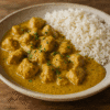 Bol de curry de poulet crémeux et riz basmati sur une table rustique. Épices aromatiques et texture savoureuse.