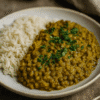 Plat de lentilles épicées avec riz blanc sur assiette, garni de coriandre fraîche, sur table en bois rustique.