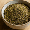 Bol de poivre vert moulu sur une table en bois, capturant la texture et les nuances naturelles de l'épice.