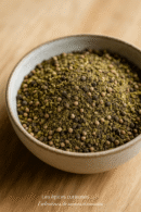 Bol de poivre vert moulu sur une table en bois, capturant la texture et les nuances naturelles de l'épice.