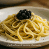 Assiette de pâtes tagliatelles al dente garnies de truffes noires, servie sur un plat blanc.