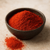 Bol de paprika en poudre rouge sur une surface beige, épice aromatique pour la cuisine.