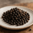 Assiette de grains de poivre noir entiers, épice essentielle pour relever saveurs et arômes des plats cuisinés.