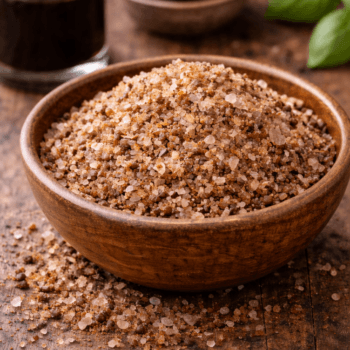 Bol de sel fumé sur table en bois avec vinaigre balsamique en arrière-plan, accentuant l'ambiance rustique.