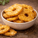 Tranches d'ananas séchées dans un bol en céramique sur une table en bois, collation saine et délicieuse.
