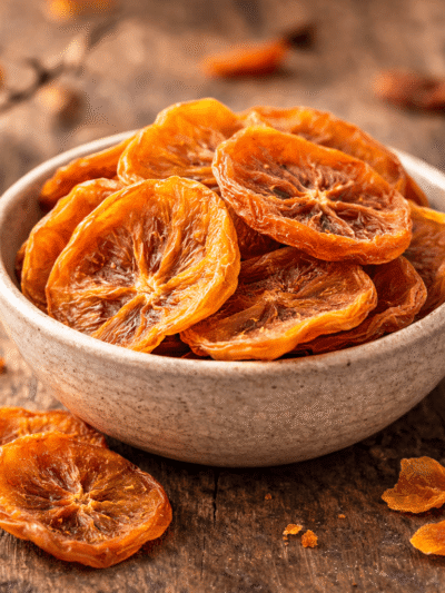 Tranches d'oranges séchées dans un bol en céramique sur une table en bois, parfaites pour un encas sain et gourmand.