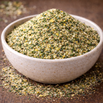 Bol rempli de gomasio aux graines de sésame et épices sur une table en bois.