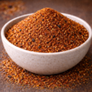 Bol de mélange d'épices rouges sur une table en bois, idéal pour rehausser les saveurs des plats.