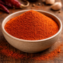 Bol de paprika en poudre sur une table en bois, avec des piments rouges et de l'ail en arrière-plan. Spécialité épicée.